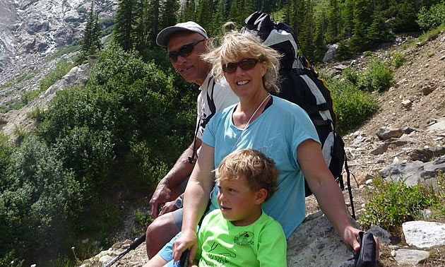 A man, woman, and child look at the camera while sitting on a mountain trail.