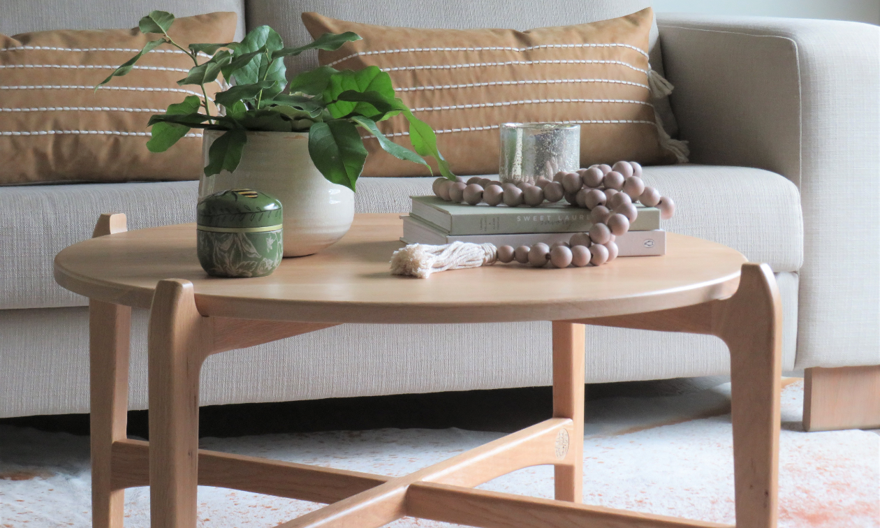 A curvy light brown coffee table has a green plant and beads on top of it. 