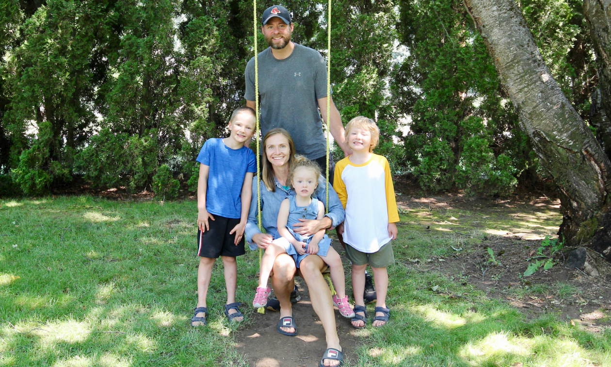 Trent and Emily Mason pose with their three children on a swing in the shade. 