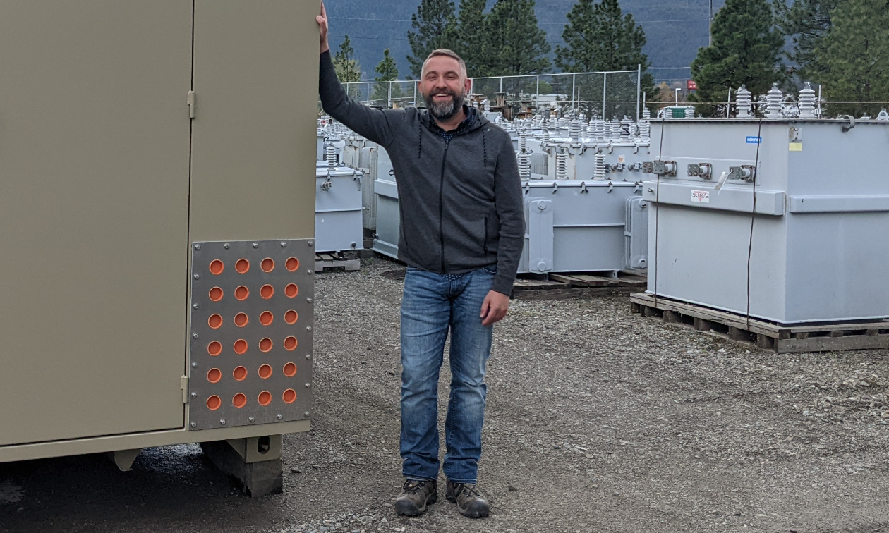 David Evdokimoff smiles while placing a hand on industrial equipment at Boundary Electric. 