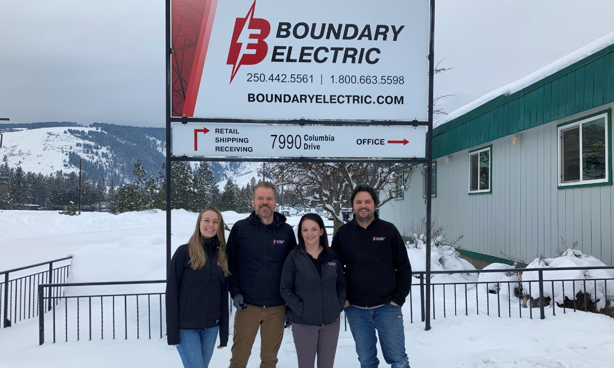 Four employees stand in front of a Boundary Electric sign in Grand Forks, B.C.
