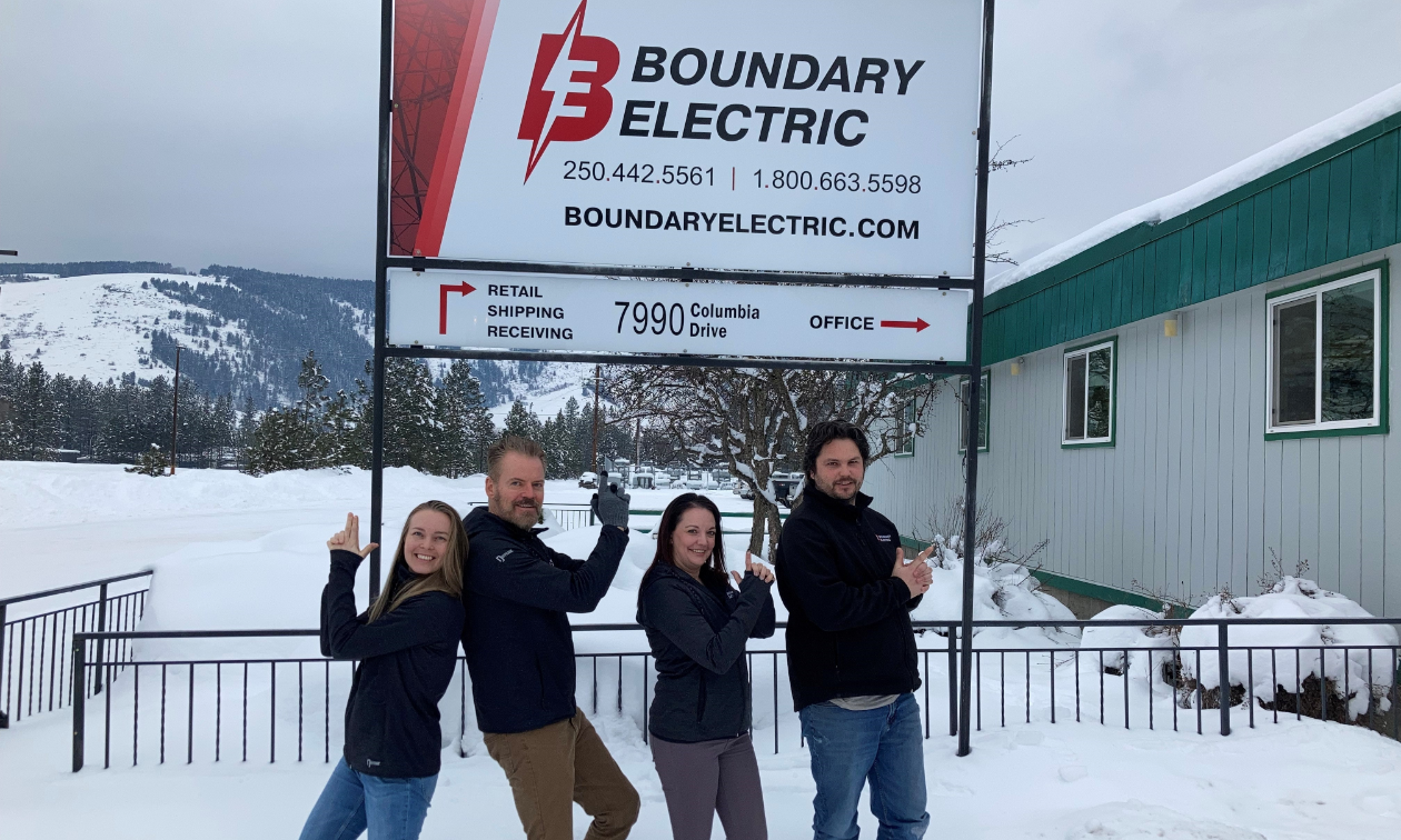 Four employees pose back-to-back in front of a Boundary Electric sign. 