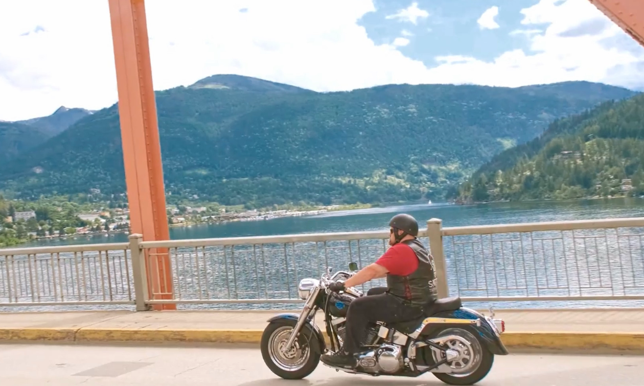 Brad Pommen rides a Harley-Davidson Fat Boy motorcycle over an orange bridge in Nelson, B.C.