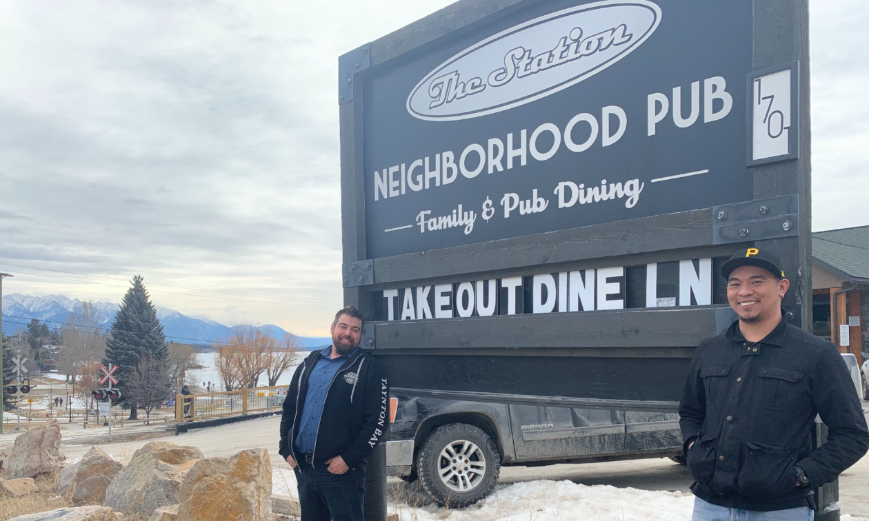 Chris Policar and Ryan “Butter” Karl stand in front of a sign that reads The Station Pub. 