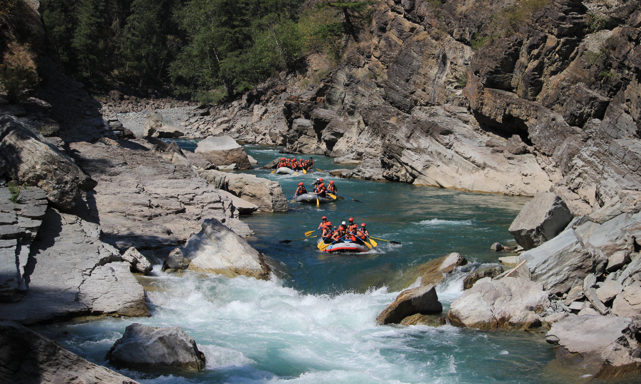 3 rafts cruise down a river filled with people wearing orange life jackets. 