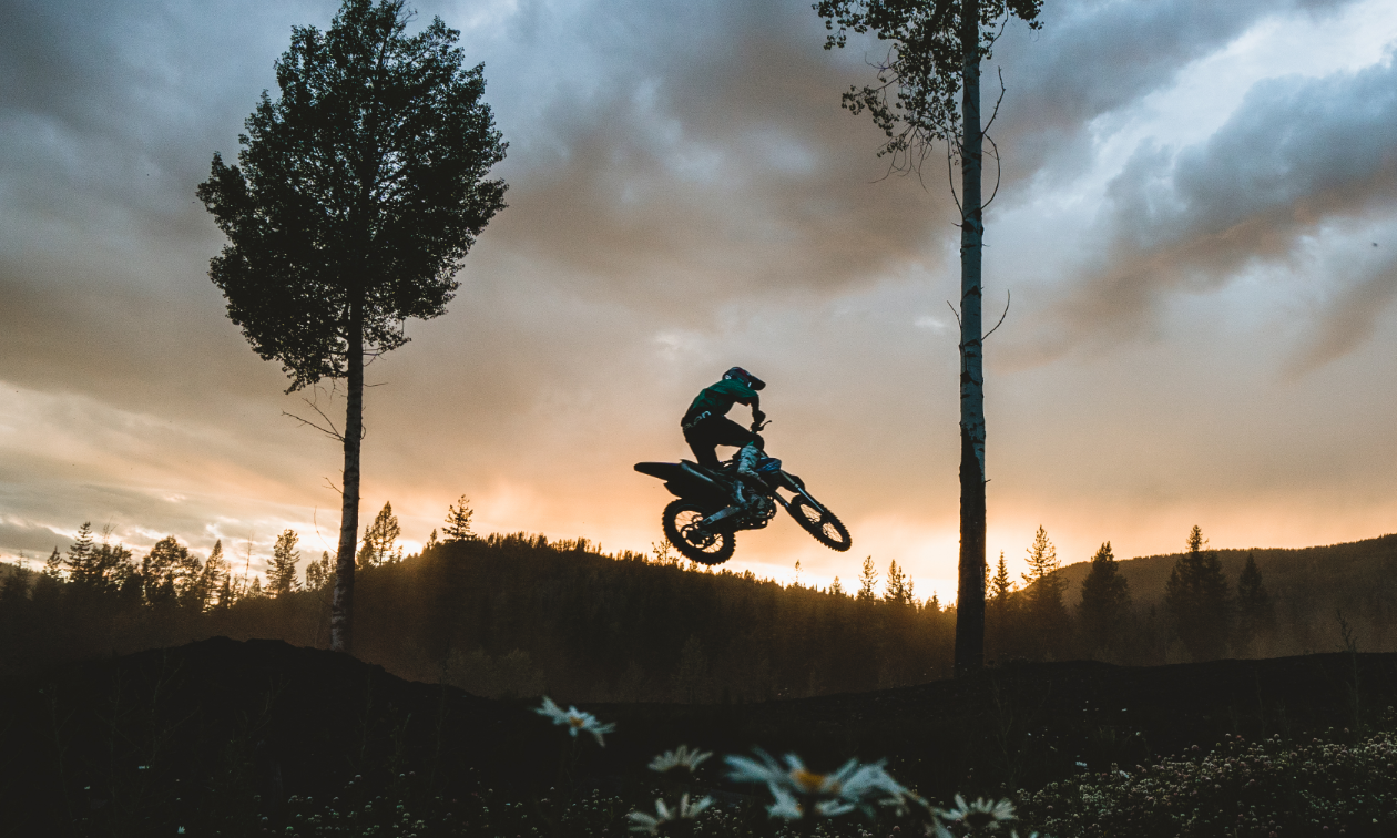 A dirt bike rider gets big air off a jump on the Kootenay Motocross track at sunset.