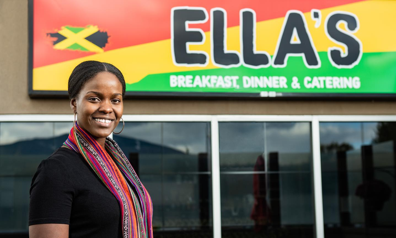 Aleitha Harvey smiles in front of her sign for her restaurant, Ella’s. 