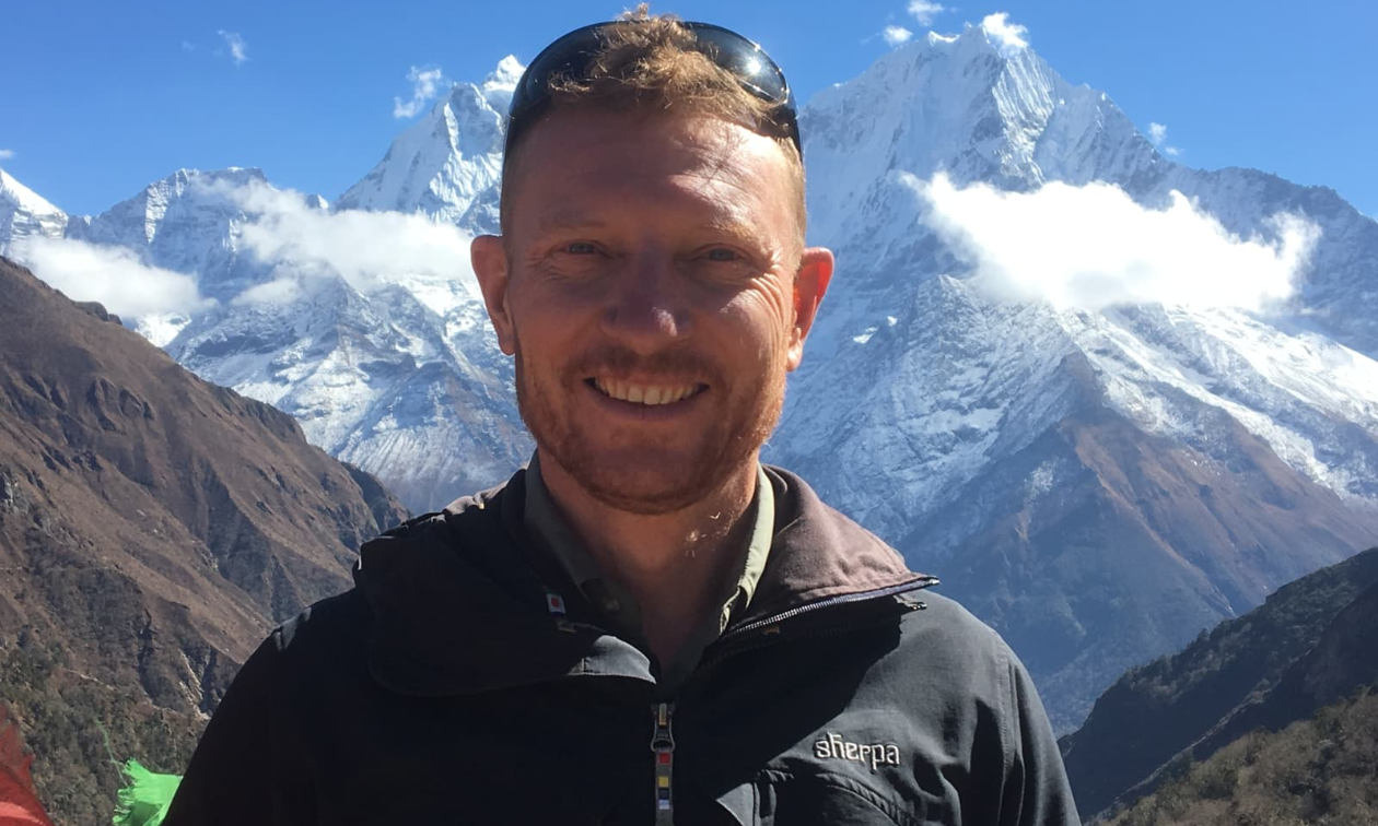 Eric Ridington smiles at the camera. Tall mountains peak in the distance.