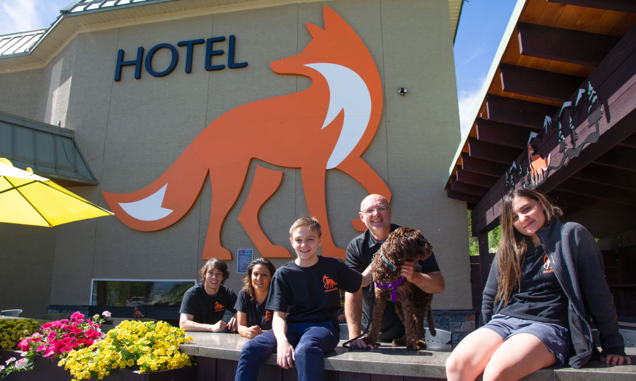 (L to R) Mackenzie, Marina, Jayden, Jeremiah and Maya Pauw in front of a hotel with a big bright orange image of a fox. 