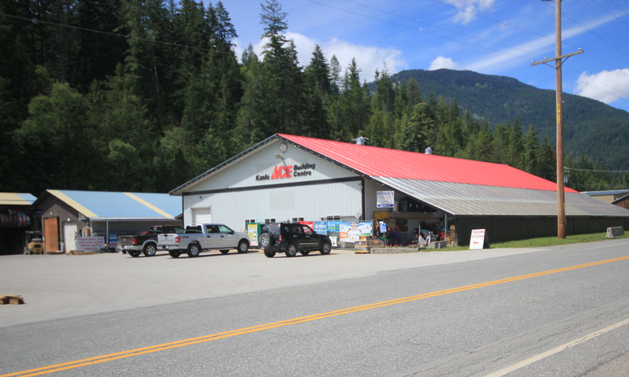 Kaslo Building Supplies is a white building with a red roof in the shade of the mountains in Kaslo, B.C.