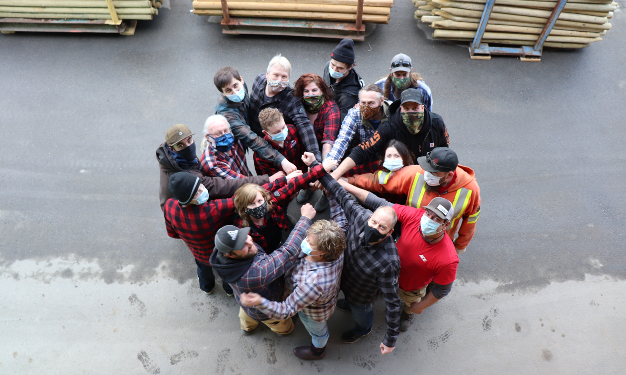 Jeff Davie (lower right with black mask), his wife, Monica Davie (very bottom, to the left of Jeff), and the team at Kaslo Building Supplies pose for a top-down photo where the group is in a circle and everyone is wearing a mask.