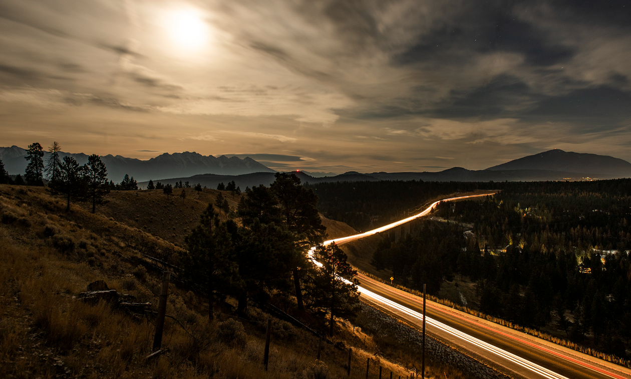 The mountains surrounding Cranbrook and the Cranbrook-Kimberley highway with streaks of light zooming across it. 