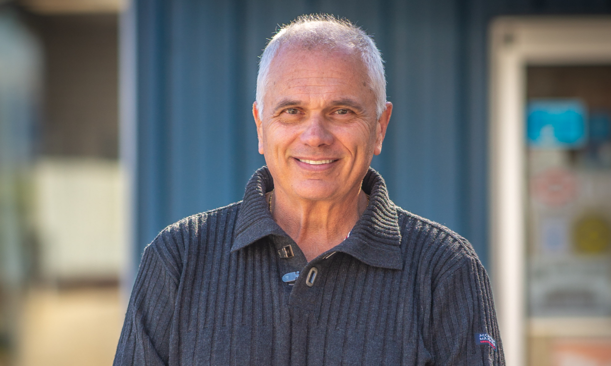 Mario DiBella has light white hair and wears a grey shirt. 