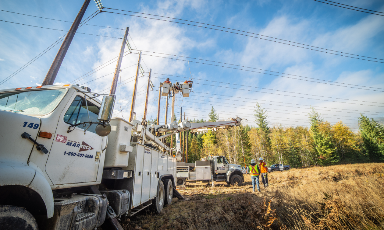 A Martech truck next to several large power poles. 