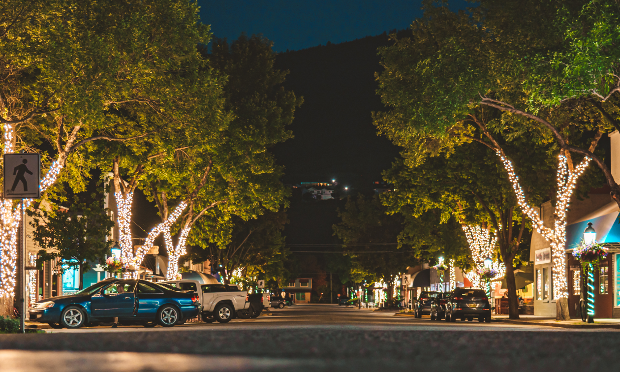 A main street in Grand Forks, B.C., is lit up with white Christmas lights wound around trees on both sides of the street. 