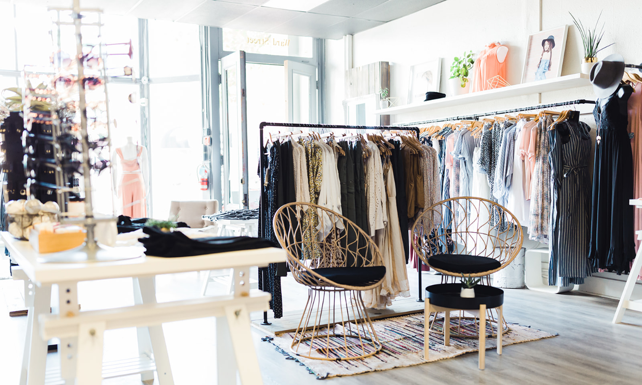 Wicker chairs are situated in front of a rack of clothing inside Scout Clothing. 