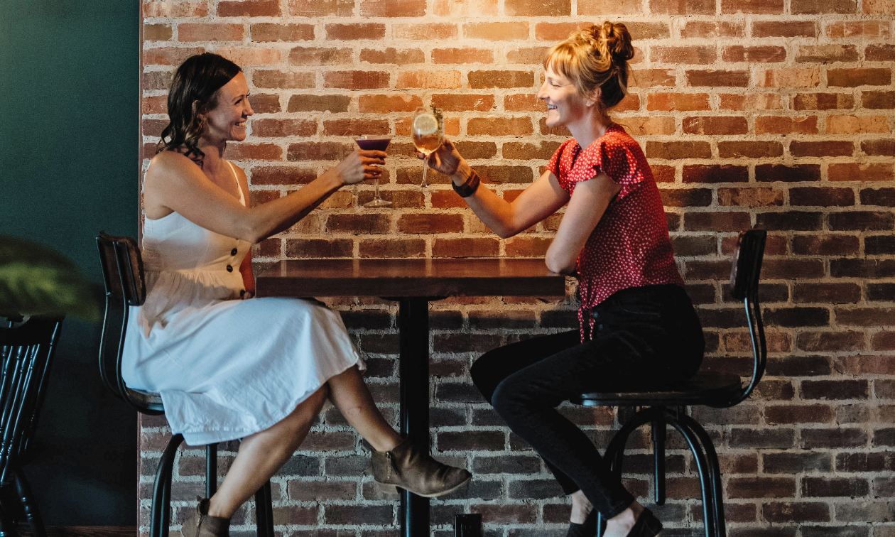 Ella Harris and Breanna Fast sit down at a table to share a drink in front of a brick wall at The Hourglass in Kimberley, B.C. 