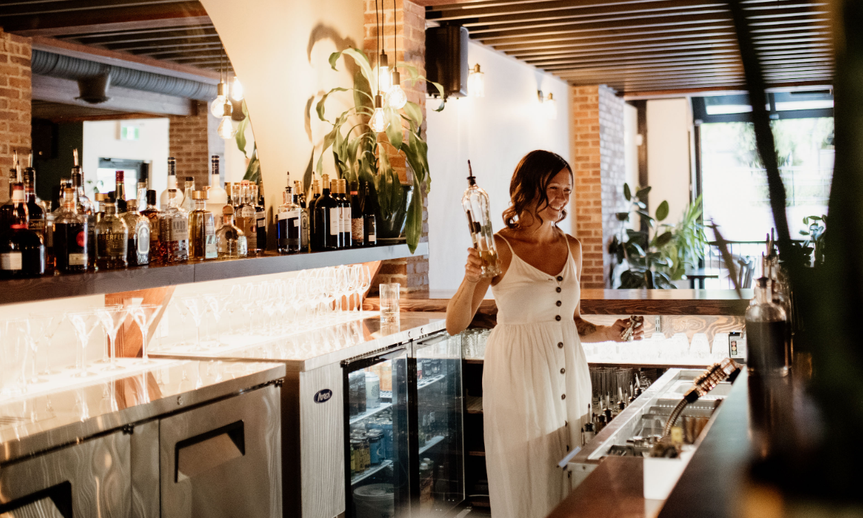 Ella Harris mixes a drink at The Hourglass while wearing a white dress.