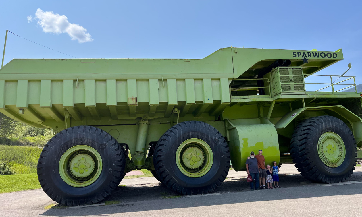 The green Terex Titan dump truck is parked with John, Kyle, Annabelle, and Gus Born standing in front of it. 