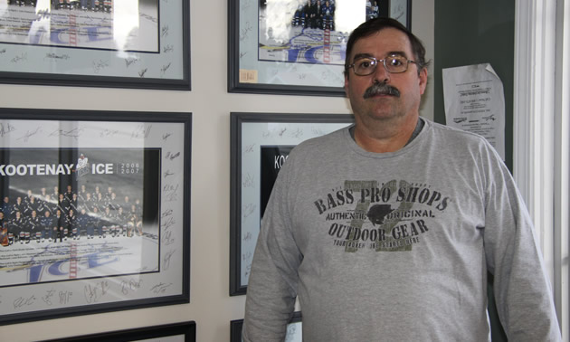 Middle-aged man wearing  a grey sweatshirt stands in front of a wall of framed photos