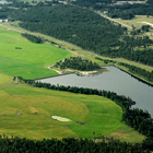 An aerial view of lush farmland with a pond and the mountains in the photo. 