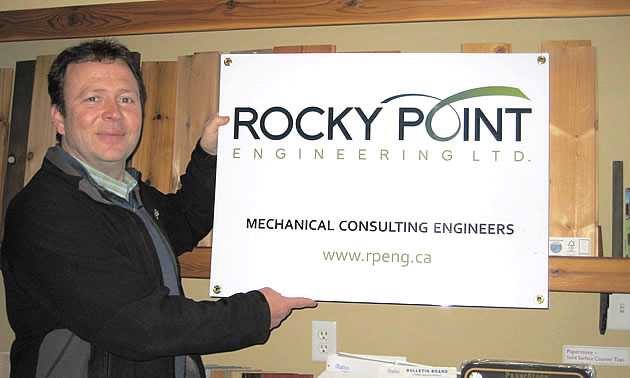 A man stands holding a sign for Rocky Point Engineering.