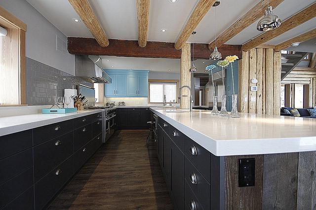 A combination of modern and rustic kitchen.  The lower cabinets are dark with white countertops.  The few upper cabinets are in aqua blue.  Ceiling beams are old reused barn wood. 
