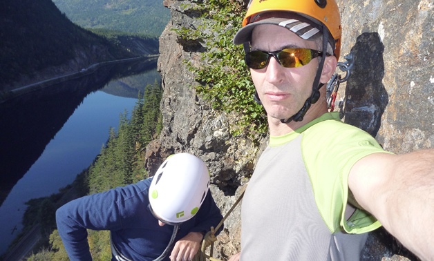 Close-up of two rock climbers on a steep rock face, with a narrow stretch of water in the background 