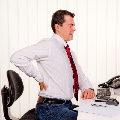 A man grabs at his back in pain while sitting at a desk