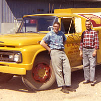 Two men standing beside a fuel truck. 