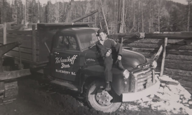 An old black and white photo of a man standing by an old truck. 