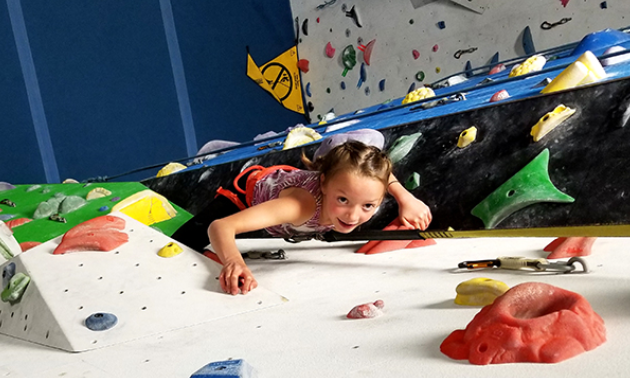 A child climbs up a colourful wall inside Arq Mountain Centre. 

