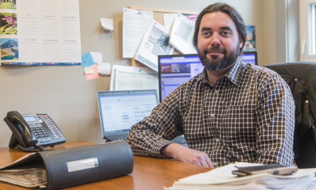 Brad Parsell sits at his desk next to a binder, a phone and a computer.