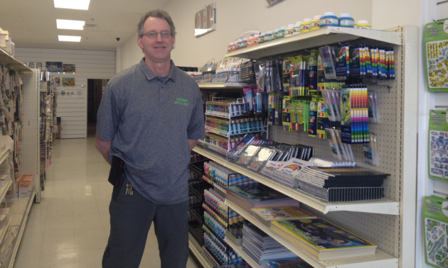 Fred Searle is standing in the crafts store near a row of paints and stretched canvases.