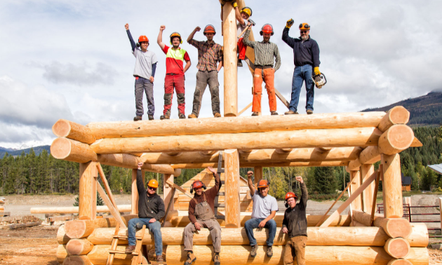 A group of carpenters hold up their fists on a log building.