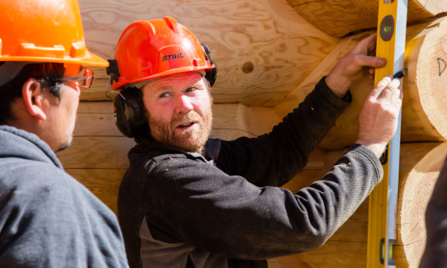 Dave Stonehouse uses a level and makes a mark on a log wall.