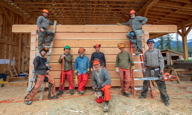 Carpenters line up inside a log building to pose for a photo.