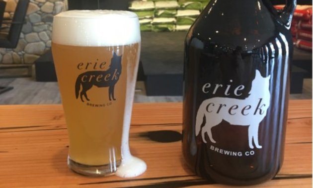 A glass and growler full of beer on a table with Erie Creek Brewing Company’s logo on the front.