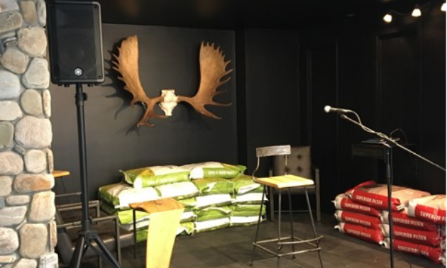 A speaker on a stand next to a chair and microphone with antlers placed on the wall behind the stage.