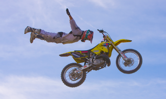 A rider flies through the air while completely letting go of his yellow dirt bike.