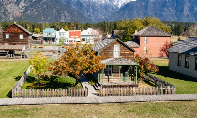 1890s-style homes and buildings reside in a rustic-looking environment with trees changing colours in fall.