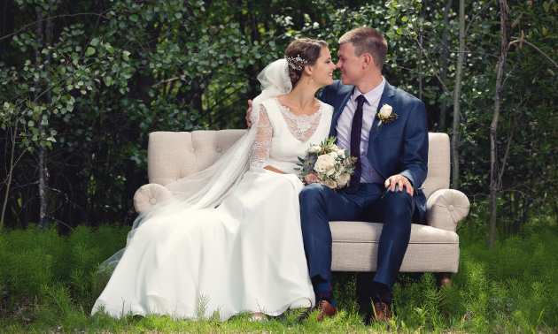 A married couple sits on a modern couch in the woods