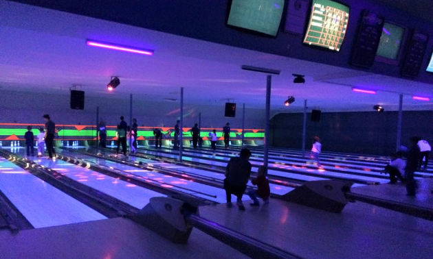 Children bowl at Juniper Lanes under purple lighting.