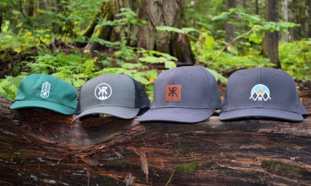 Four beige and green hats are lined up on a log in the woods.