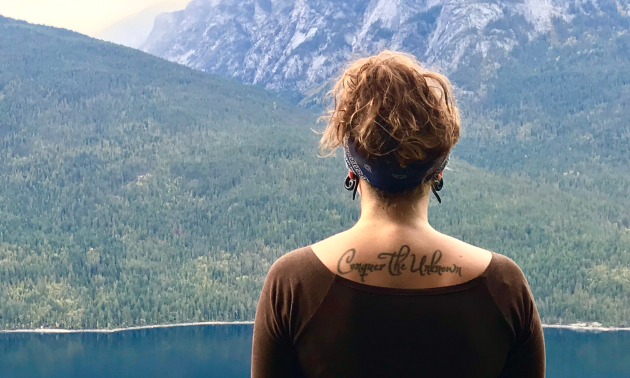 Kornelsen has her back to the camera as she looks out to a lake and mountains.