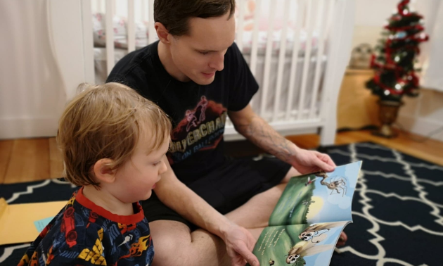 A father reads to his son on the floor. 