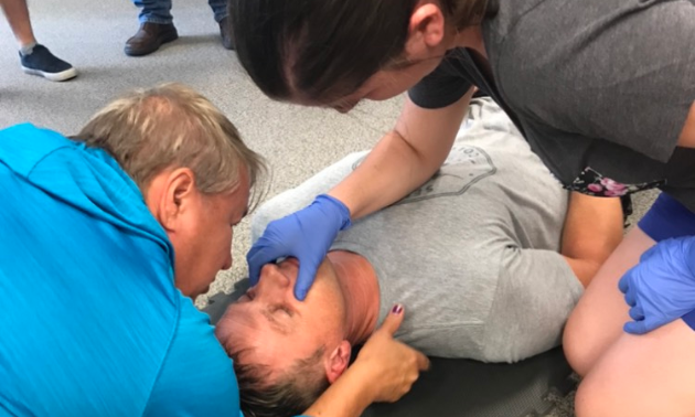 Two people perform CPR on a man on his back. 