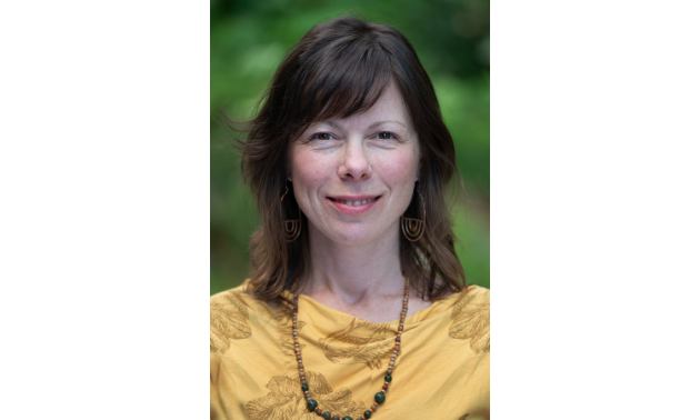 Melissa Welsh smiles, wearing a yellow shirt and a necklace.