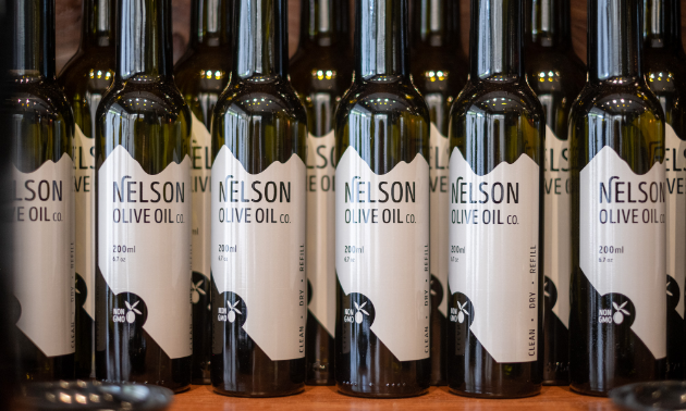 A line of dark green bottles with white Nelson Olive Oil labels on them.