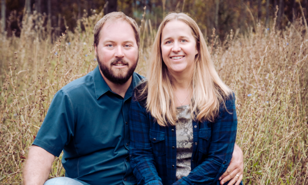 Remi and Shannon Cardinal sit in a field.